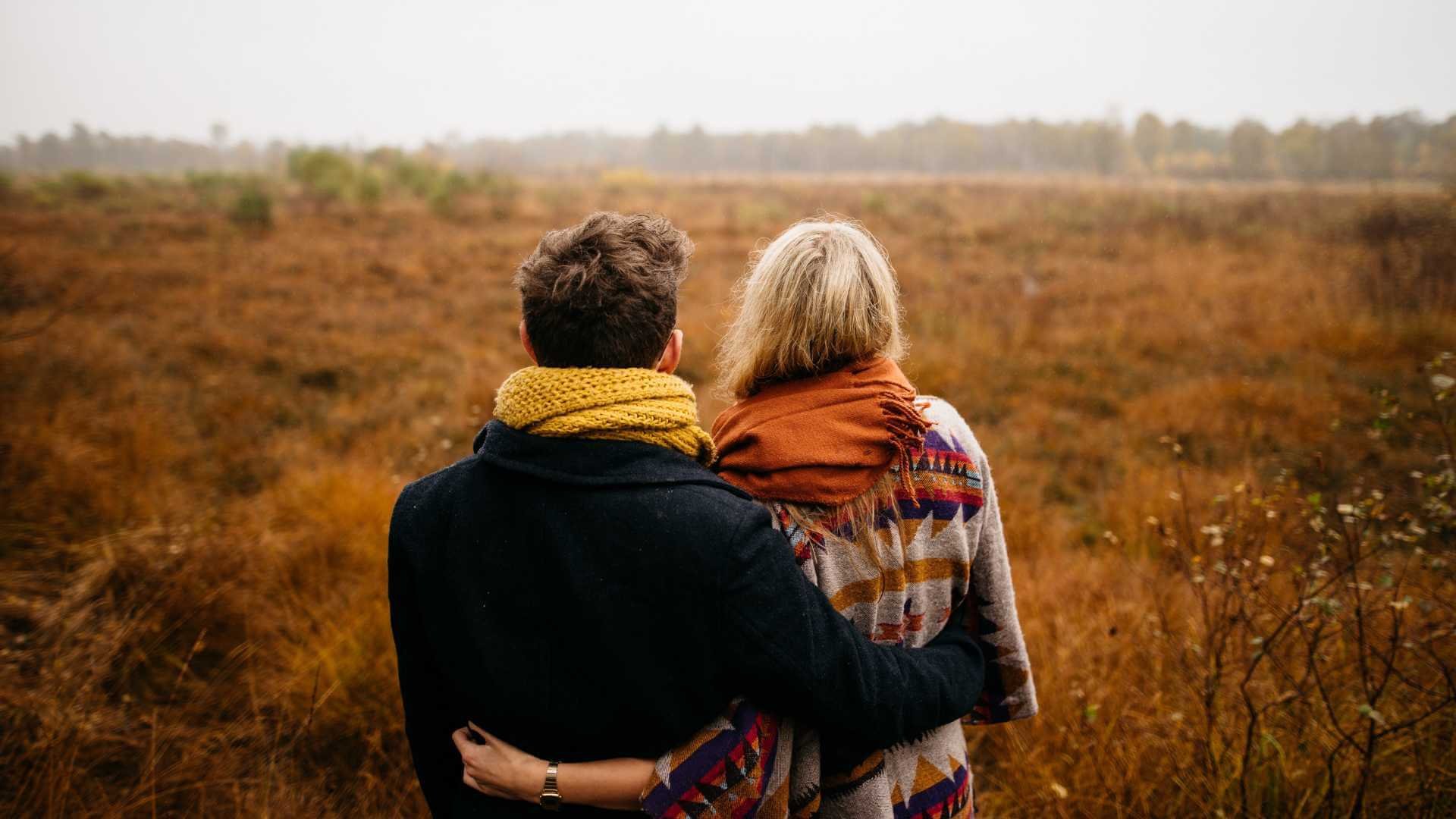 A couple stands in a field of autumn leaves