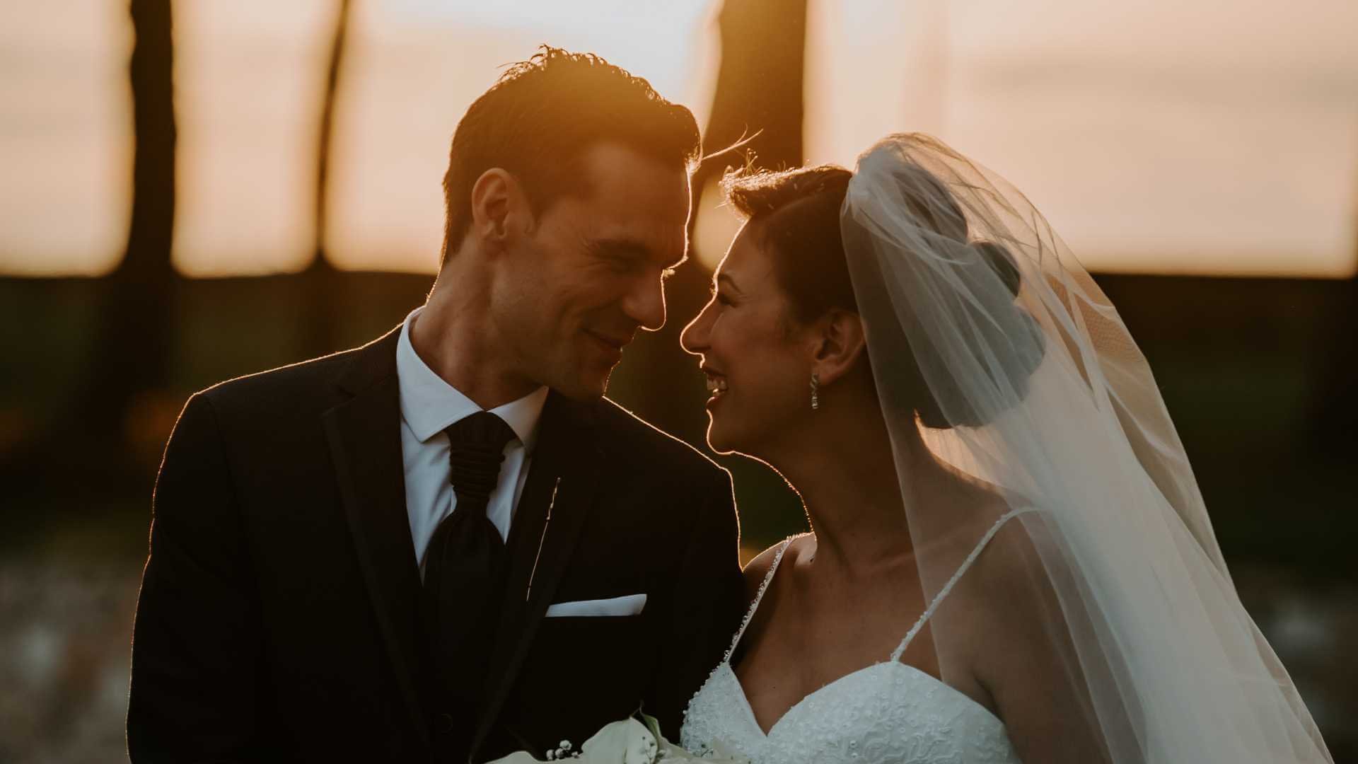 A happy bride and groom smiling at each other during a beautiful sunset.