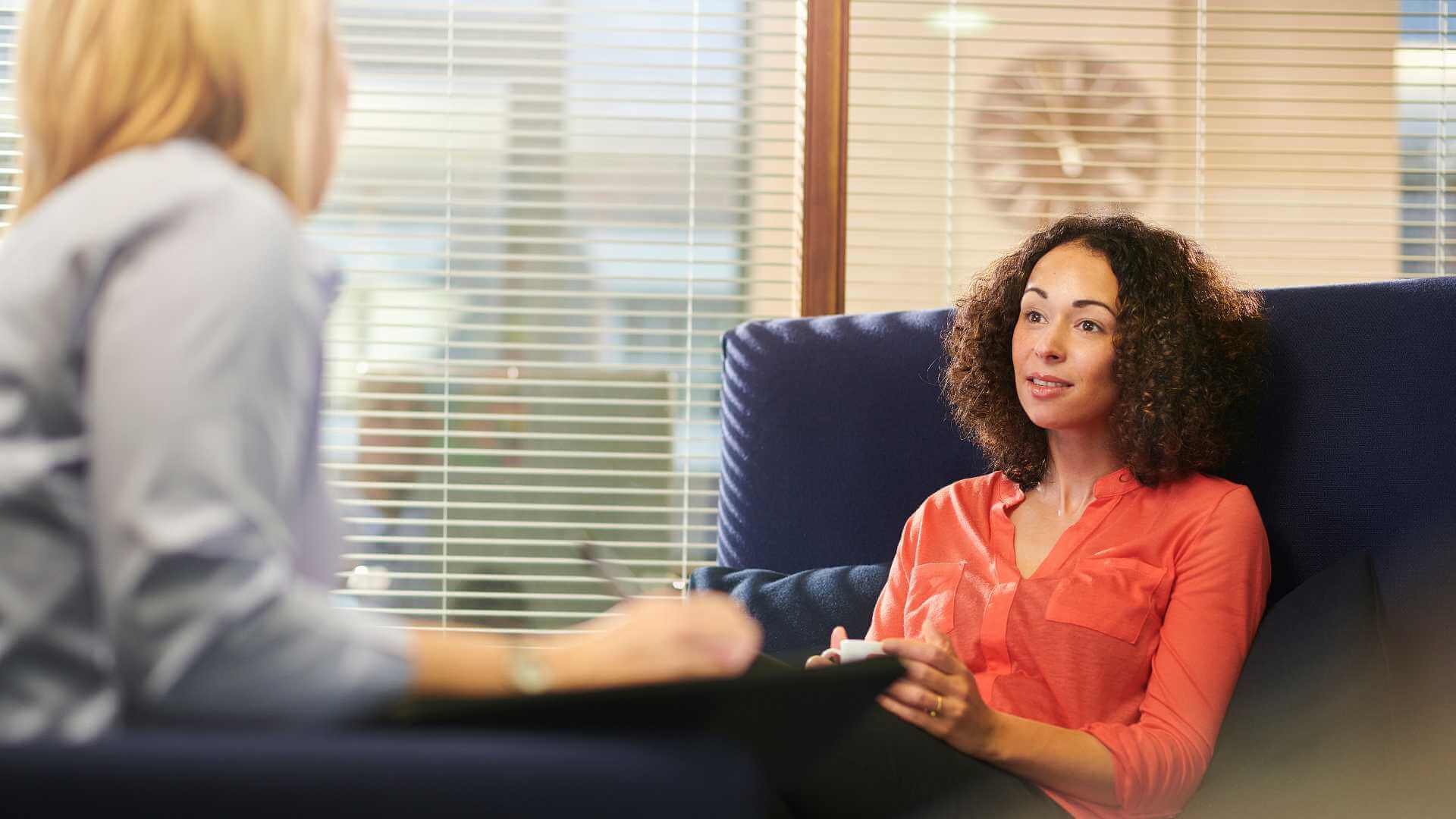 A woman chatting with another woman on a couch.