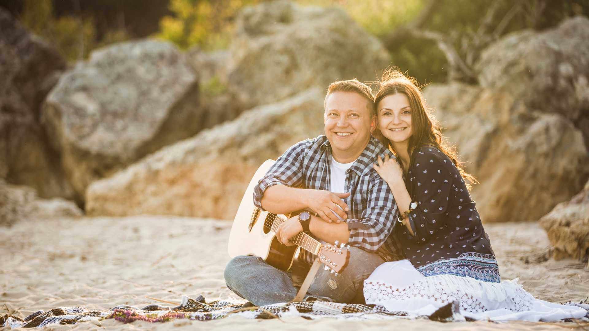 A couple playing guitars on the beach, enjoying the beautiful scenery and music.