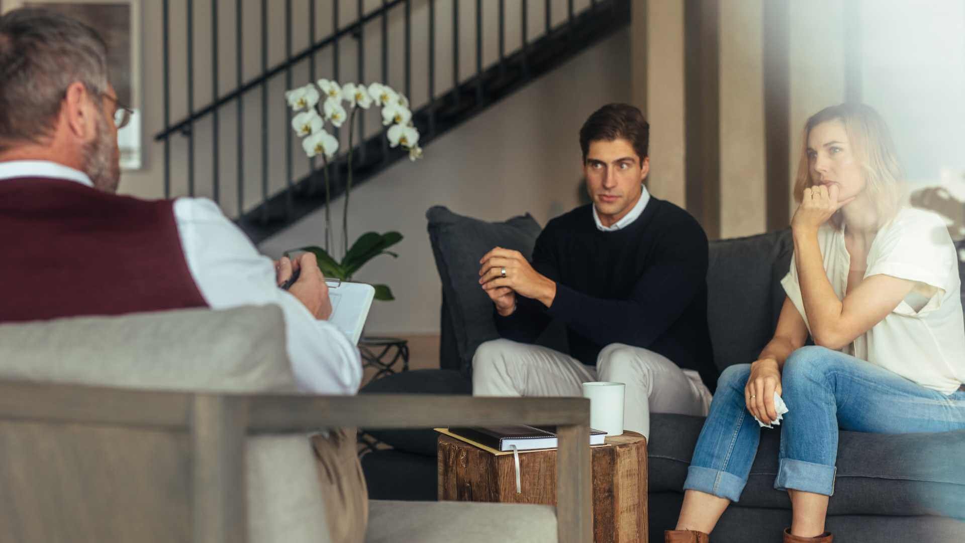 A man and woman talking to another man on a couch.
