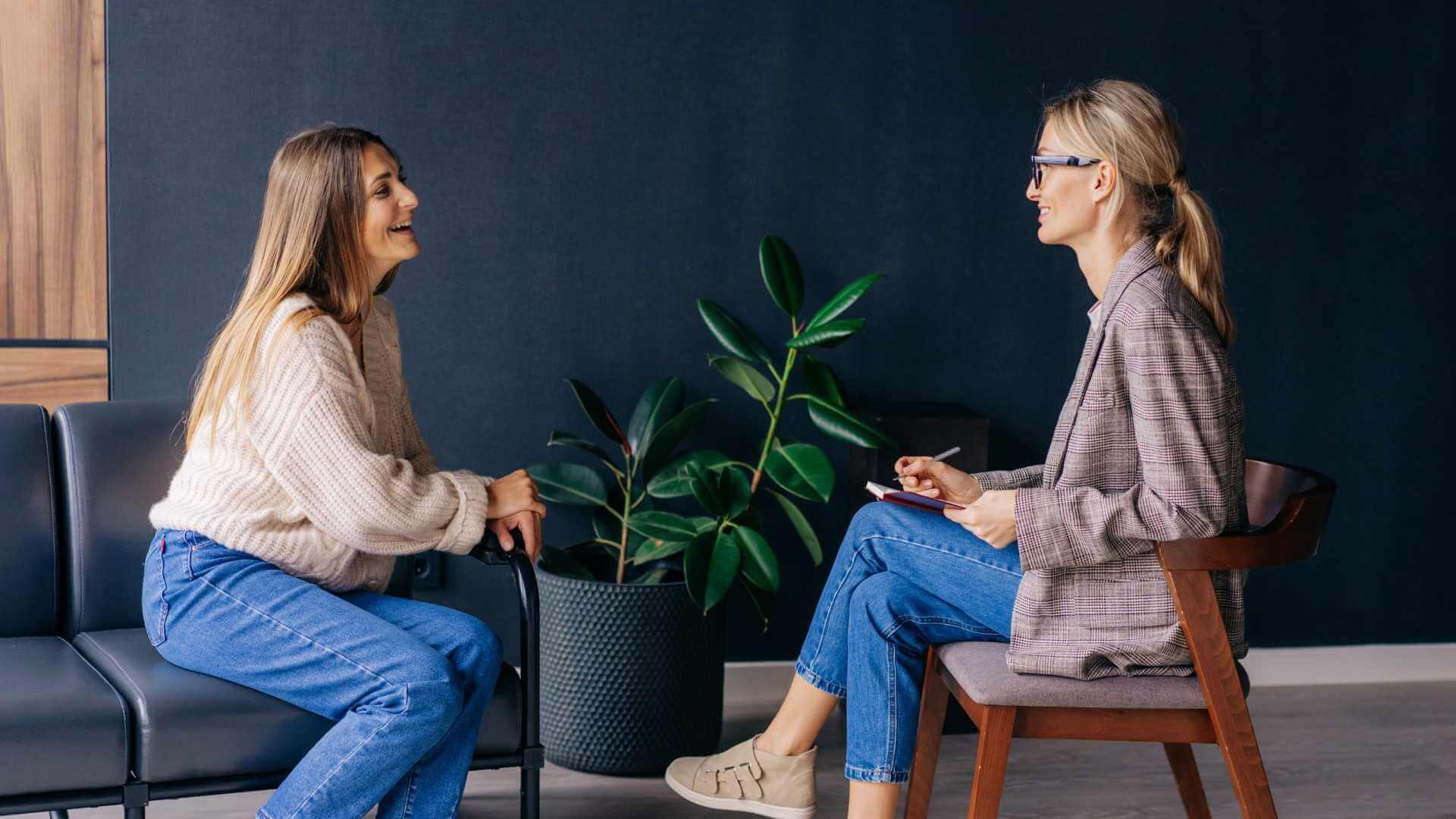 Two women sitting on a couch chatting with each other.